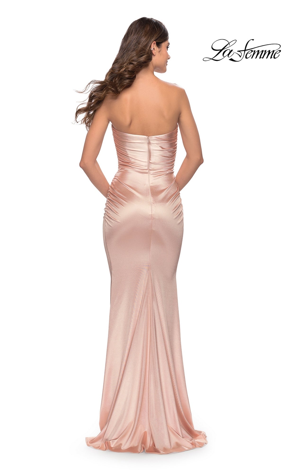 A woman models the Simple Strapless Long La Femme Prom Dress 31189 in light pink satin with a fitted, ruched back and slight train, shown from behind. The La Femme logo appears in the upper right corner.